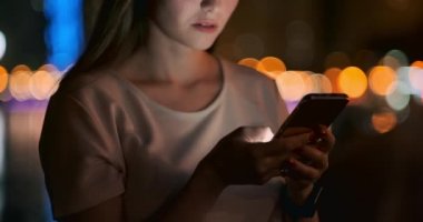 Gece şehrinin arka planında genç bir kız akıllı telefon ekranına bakıyor