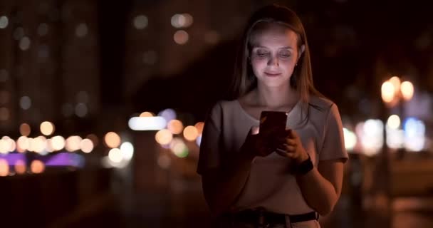Een jong meisje op de achtergrond van de nacht stad kijkt naar het scherm van de smartphone — Stockvideo