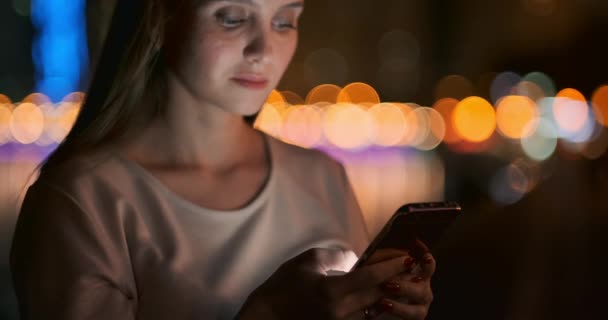 Une jeune fille sur le fond de la ville de nuit regarde dans l'écran du smartphone — Video