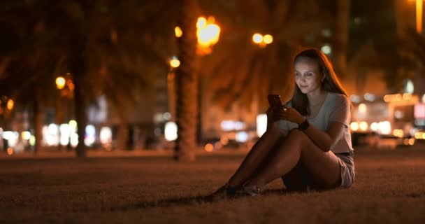 밤 도시의 배경에 어린 소녀는 스마트 폰 화면에 보인다 — 비디오