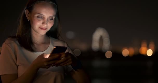 Ночью молодая девушка держит в руках смартфон и смотрит на экран. — стоковое видео