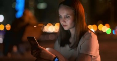 Bokeh gece şehir genç kadın akıllı telefon ekranına bakıyor