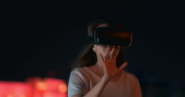 Jonge vrouw in virtual reality bril in de nacht stad beweegt haar handen — Stockvideo