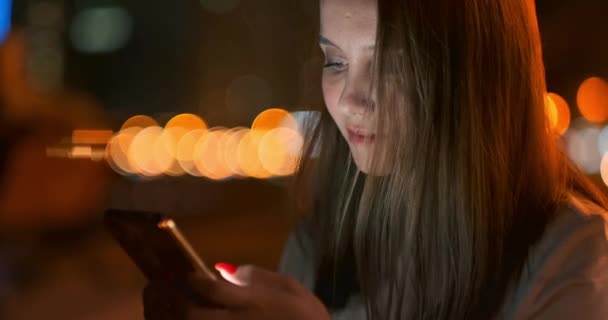 Jeune fille dans la ville de nuit écrit des messages texte dans un smartphone — Video
