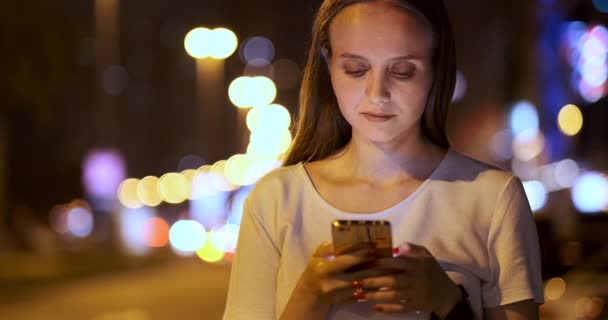 Fiatal lány az éjszakában város szöveges üzeneteket ír egy okostelefonon — Stock videók