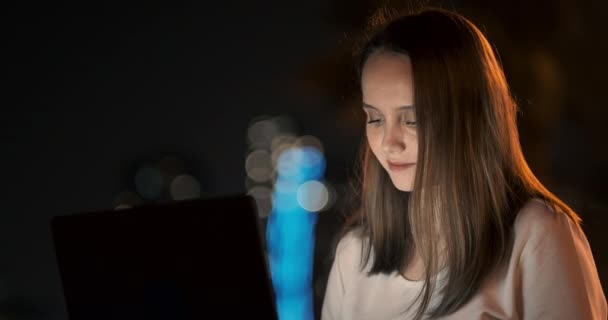 Žena developer sedí v noci v parku ve městě a píše kód při pohledu na obrazovce notebooku — Stock video