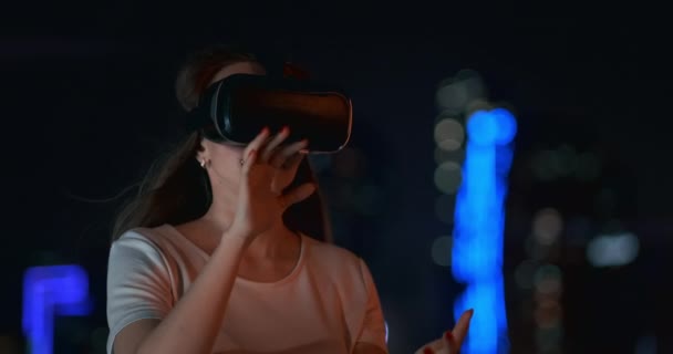 Ung kvinna i virtual reality glasögon i natten staden flyttar händerna — Stockvideo