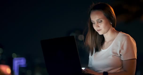 Jovem mulher noite de verão sentado na grama com laptop na cidade — Vídeo de Stock