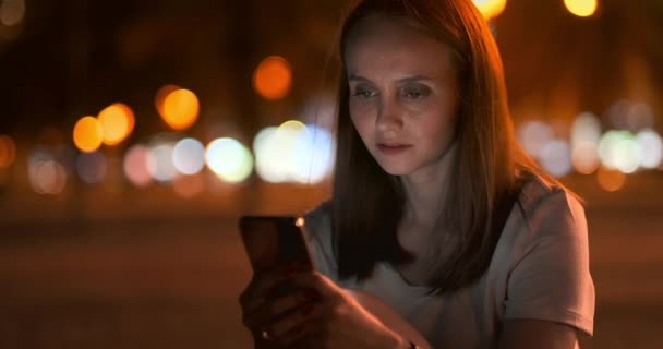 Jeune fille dans la ville de nuit écrit des messages texte dans un smartphone 