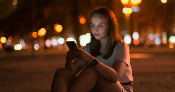 Giovane ragazza nella città di notte scrive messaggi di testo in uno smartphone — Video Stock