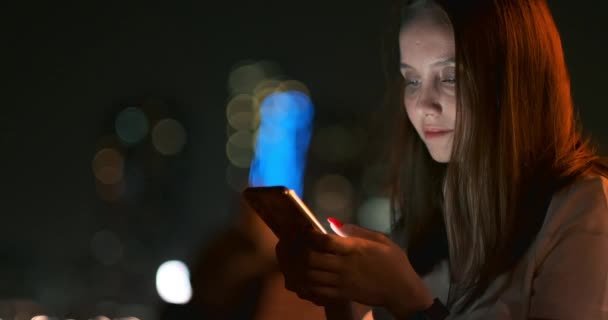Pada malam hari, seorang gadis muda memegang smartphone di tangannya dan melihat layar — Stok Video