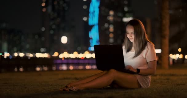 Donna sviluppatore si siede nel parco di notte in città e scrive codice guardando lo schermo del computer portatile — Video Stock