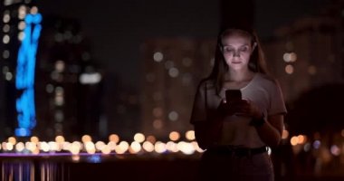Bokeh gece şehir genç kadın akıllı telefon ekranına bakıyor