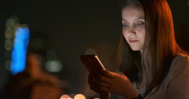 Gece şehrinin arka planında genç bir kız akıllı telefon ekranına bakıyor