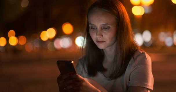 Bokeh noche ciudad joven mujer mirando en la pantalla del teléfono inteligente — Vídeos de Stock