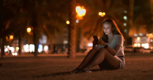 Chica joven en la ciudad nocturna escribe mensajes de texto en un teléfono inteligente — Vídeos de Stock