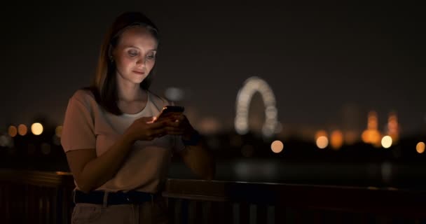 Bokeh νυχτερινή πόλη νεαρή γυναίκα κοιτάζοντας στην οθόνη του smartphone — Αρχείο Βίντεο