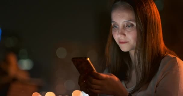 Mujer joven sentada por la noche en la ciudad con smartphone — Vídeo de stock