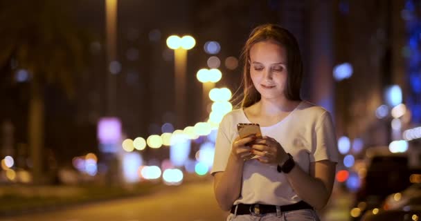 Jonge vrouw 's nachts in de stad belt een taxi via smartphone — Stockvideo