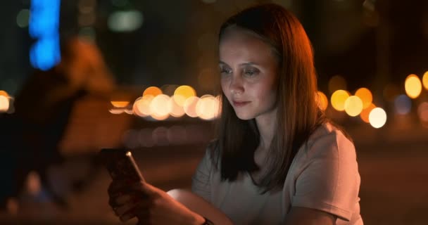 Young girl in the night city writes text messages in a smartphone — Stock Video