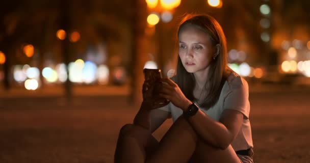 스마트폰 화면을 바라보는 보케 나이트 시티 젊은 여성 — 비디오