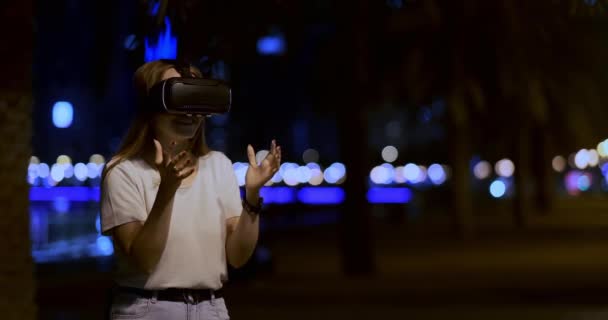 Jonge vrouw in virtual reality bril in de nacht stad beweegt haar handen — Stockvideo