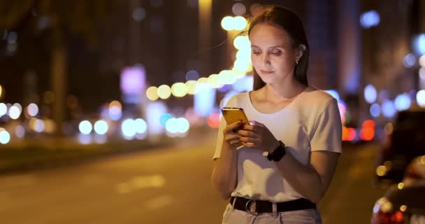 Fiatal lány az éjszakában város szöveges üzeneteket ír egy okostelefonon — Stock videók