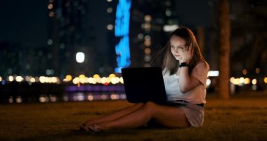 Geceleri dizüstü bilgisayarı olan genç bir kız öğrenci şehirde yazı yazıyor.