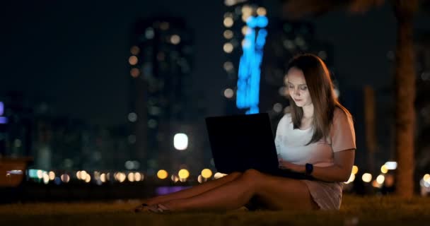 Giovane designer ragazza che lavora a distanza sul computer portatile fuori sotto le palme di notte — Video Stock