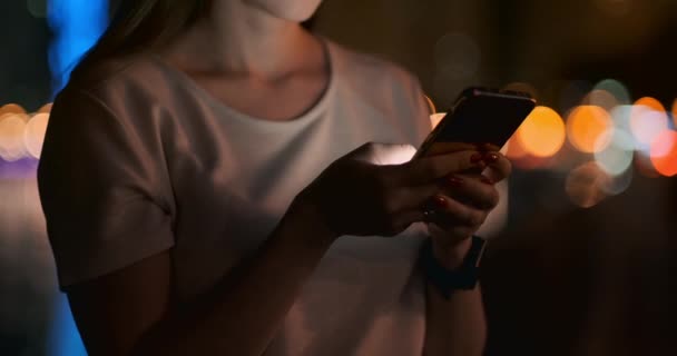 Крупный план мобильного телефона в руках девушки в городе ночью — стоковое видео