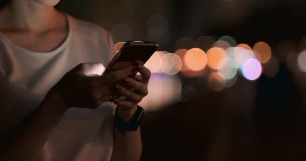 Primer plano de un teléfono móvil en manos de una chica en la ciudad por la noche — Vídeos de Stock