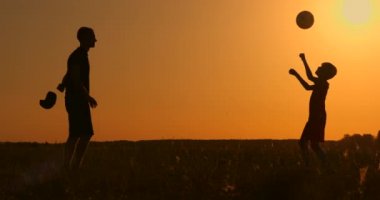 Baba ve oğul parlak bir güneş, ağır çekim çekim zemin karşı günbatımı, siluetleri parkta futbol oynayan