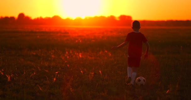 Niño jugador de fútbol con una pelota al atardecer en el campo corriendo desde la cámara — Vídeo de stock