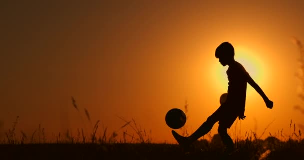 Silueta de un niño jugando fútbol o fútbol en la playa con hermoso fondo de atardecer Infancia, serenidad, deporte, concepto de estilo de vida — Vídeos de Stock