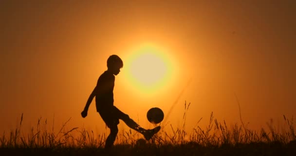 Silueta de futbolista niño, practicando con la pelota, la puesta del sol Hora dorada, cámara lenta . — Vídeo de stock