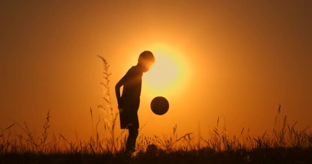 Silueta de futbolista niño, practicando con la pelota, la puesta del sol Hora dorada, cámara lenta . — Vídeos de Stock