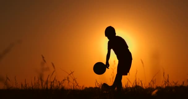 美しい夕日の背景子供時代、静けさ、スポーツ、ライフスタイルの概念を持つビーチでサッカーやサッカーをしている少年のシルエット — ストック動画