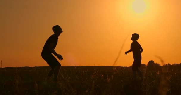 Vater und Sohn beim Fußballspielen im Park bei Sonnenuntergang, Silhouetten vor dem Hintergrund einer strahlenden Sonne, Zeitlupenschießen — Stockvideo