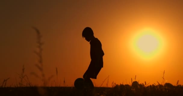 Silhouette di un ragazzo che gioca a calcio o calcio in spiaggia con un bellissimo sfondo al tramonto Infanzia, serenità, sport, concetto di stile di vita — Video Stock