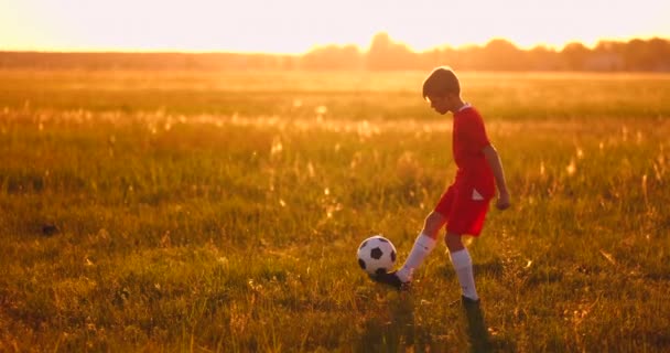 Хлопчик-футболіст на заході сонця жонглює м'яч у полі — стокове відео