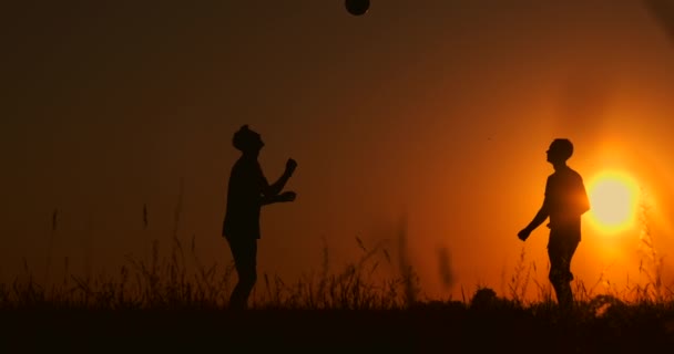Два хлопці грають у футбол на заході сонця. Силует дітей, які грають з м'ячем на заході сонця. Поняття щасливої сім'ї — стокове відео