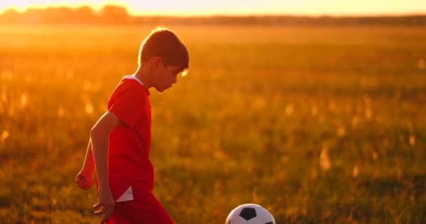 Chłopiec piłkarz o zachodzie słońca żonglerka piłkę w polu — Wideo stockowe