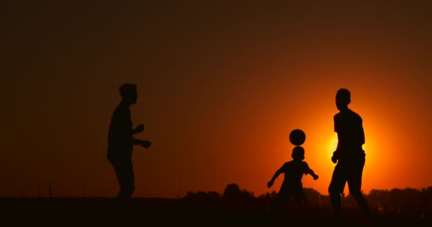 Três rapazes a jogar futebol ao pôr-do-sol. Silhueta de crianças brincando com uma bola ao pôr do sol. O conceito de uma família feliz — Vídeo de Stock