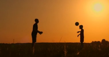 Baba ve oğul parlak bir güneş, ağır çekim çekim zemin karşı günbatımı, siluetleri parkta futbol oynayan