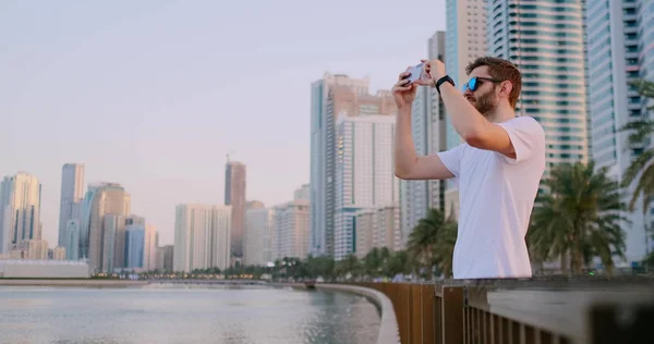 Чоловік влітку стоїть на набережній, сфотографований на смартфоні ландшафту міста — стокове фото