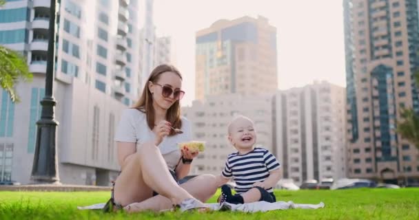 In de zomer in het Park moeder voedt het kind van de container lunch — Stockvideo