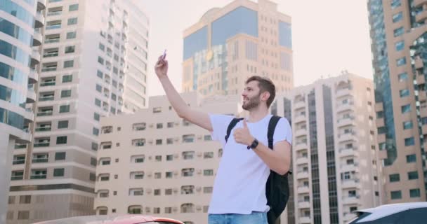 Un joven con una mochila se hace una selfie en la ciudad — Vídeos de Stock