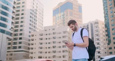 Elinde sırt çantası ve akıllı telefon olan genç bir adam.