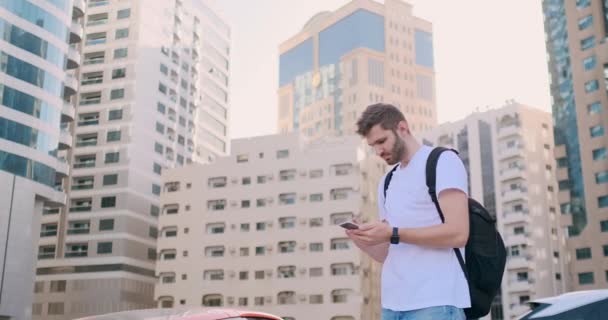 Молодой человек с рюкзаком и смартфоном в руках — стоковое видео