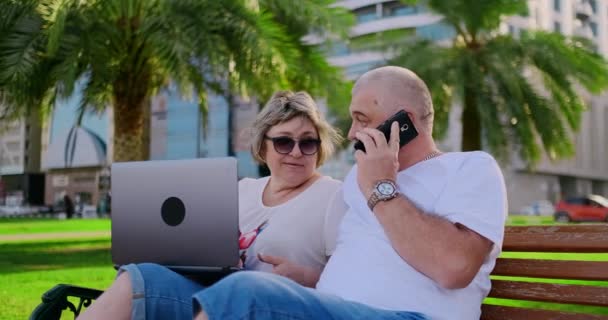 Starsza para za pomocą laptopa w parku w słoneczny dzień — Wideo stockowe